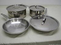 Full set including 2 pots with lids, 2 frying pans one with lid laid out on surface.