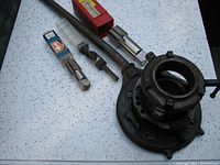Photo showing the adjustable pipe die with long handle and included accessories on a white surface. Accessories include drill bit and pipe taps in cases.