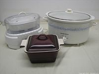 Photo showing all three items in the lot: the Sunbeam Instant Steamer, Hamilton Beach slow cooker, and Presidents Choice casserole dish.