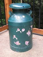 Full view of the green painted metal milk can with floral paper appliques, showing overall shape and condition.