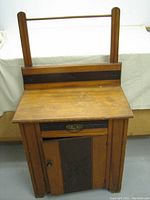 Front view of vintage Eastlake washstand showing top surface, towel bar, single drawer with metal pull, and single door with carved panel and knob.