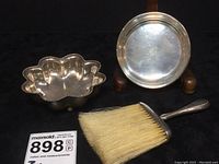 Photo of footed sterling silver bowl with scalloped bead edge, round plain bowl and table brush with natural bristles on a black background.