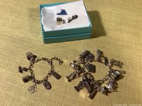 Two charm bracelets, one with 5 charms and one with 18 charms, along with three loose charms in a blue box