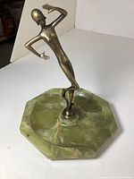 Brass dancing figurine standing on green stone base with octagonal shape, showing details of brass figure and green stone.