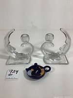 Front view showing two clear glass crescent moon-shaped candle holders and one small round ceramic tea bag plate with moon design