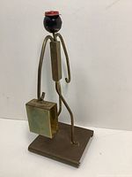 Side view of brass figurine with red cap holding brass briefcase designed as matchbox holder.