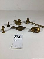 Six small brass figurines displayed on a white surface, including two ducks, a small gavel, a curled fox, and two figurines of a character wearing a hat.
