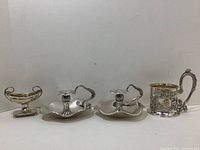All four items displayed together: salt cellar at left, pair of chamberstick candle holders center, handled cup at right.