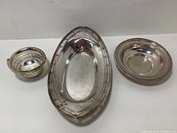 Three sterling silver pieces displayed: oval tray center, round dish right, small basket with handle left.