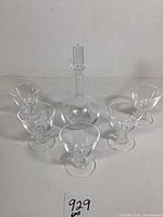 One clear glass decanter with spiral air twist stopper centered behind five matching cocktail glasses arranged in front on white background.