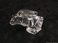 Crystal clear hand warmer in the shape of a rabbit resting on black fabric, showing side profile with visible ears and legs.