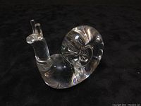 Clear crystal snail hand warmer positioned on black background showing the smooth, polished snail shape with prominent coiled shell and antennae.
