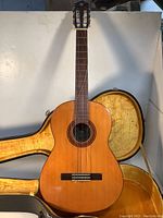 Front view of vintage Yamaha classical guitar in natural wood finish with hard case open behind it.