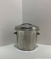 Front view of pewter miniature trash can shaped toothpick holder with lid on