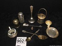 Wide photo showing entire set of 11 sterling silver table accessories on black background with lot number card.