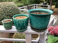 Three ceramic pots in small, medium, and large sizes arranged on a wooden railing outdoors, showing glazing and shape details.