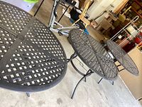Three round metal outdoor tables with lattice pattern tops and umbrella holes, legs visible, showing overall condition of tables.