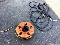 Wide shot showing both the orange reel with the yellow 30 amp RV extension cord and the separate long black extension cord.