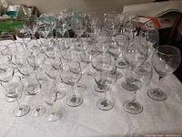 Wide view of 45 clear wine glasses arranged on table with varying heights and bowl sizes.