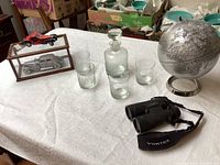 Photo showing the full lot on a white tablecloth, including the model cars on wooden display, glass decanter, four glasses, Vortex binoculars and silver globe.
