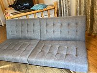 Front view of slate gray, button-tufted futon in sofa position showing the fabric and upholstery style.