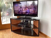 Front view showing Sony TV turned on with three curved black tempered glass shelves and wood grain laminated side panels on TV stand.