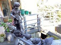 Full view of statuaries set on outdoor railing showing girl figure, raccoon, and three ducks
