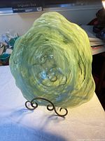 Front view of the lime green swirl glass plate on metal display stand showing wavy edges and textured swirl pattern.