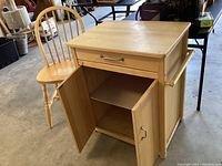Photo of oak kitchen cabinet with drawer, doors open revealing two shelves inside, and matching oak chair.