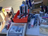 Table with paint tools showing power stripper, spray guns, paint roller tray, and drop cloth.