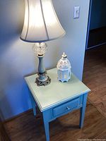 Table against wall with lamp and candle holder on top, showing pale green color and condition