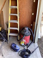 Overall view of the Shop Vac with attached hose, yellow 6 ft ladder, blue pressure washer, portable shop light, and accessories on floor.