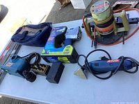 Wide view of the power tools on table showing boxed impact wrench, Black & Decker router, Ryobi sander, Drill Doctor, tool bag, sanding blocks, and accessories.
