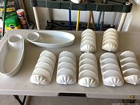 Two white oval ceramic trays with built-in salsa bowls and seven white ceramic taco holders arranged on a table.