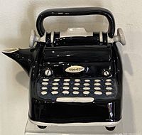 Front view of black ceramic typewriter teapot with detailed keys and handle, spout on left side
