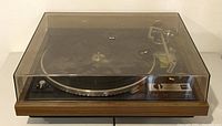 Front view with dust cover closed showing wood-tone plinth, platter and tonearm