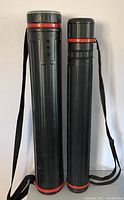 Both telescoping art tubes standing upright, showing black cylindrical bodies with red trim and attached shoulder straps.