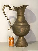 Front view of large etched brass pitcher next to soda can for scale