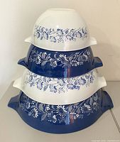 Stacked view of four vintage Pyrex Cinderella mixing bowls alternating white and blue with Colonial Mist floral design showing handles and pattern details.