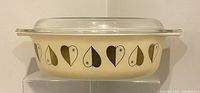 Side view of the Pyrex Golden Heart casserole dish with clear glass lid, showing heart pattern and handles