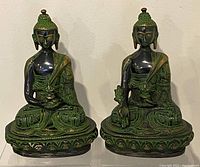 Front view of two green and black brass meditating Buddha statues seated side by side showing detailed designs on robes and faces.