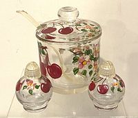 Photo of front angle of the vintage glass jar with lid and spoon, flanked by two round condiment shakers. All hand painted with cherries and floral designs.