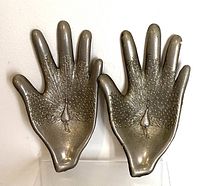 Pair of metal hand-shaped ashtrays with peacock design, front view showing embossed peacock tail feathers and body detail in the palm of each hand-shaped ashtray.