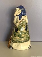 Front view of Baba Yaga witch utensil holder showing face, blue headscarf, green apron, broom, and utensil openings.
