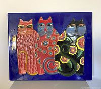 Front view of ceramic wall plaque showing three colorful cats with different patterns on blue background