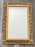 Full view of the rectangular gold-tone ornate framed mirror on floor.