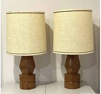 Pair of mid-century wooden table lamps with fabric shades shown side by side on white surface.
