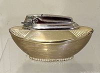 Front side view showing gold-toned table lighter with silver-tone firing mechanism on top, in Art Deco design.