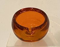 Front view of vintage Viking orb-shaped orange-reddish art glass ashtray resting on clear stand against white background