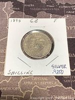 Reverse side of the 1895 Great Britain silver one shilling coin showing crowned shield with floral elements and inscriptions.
